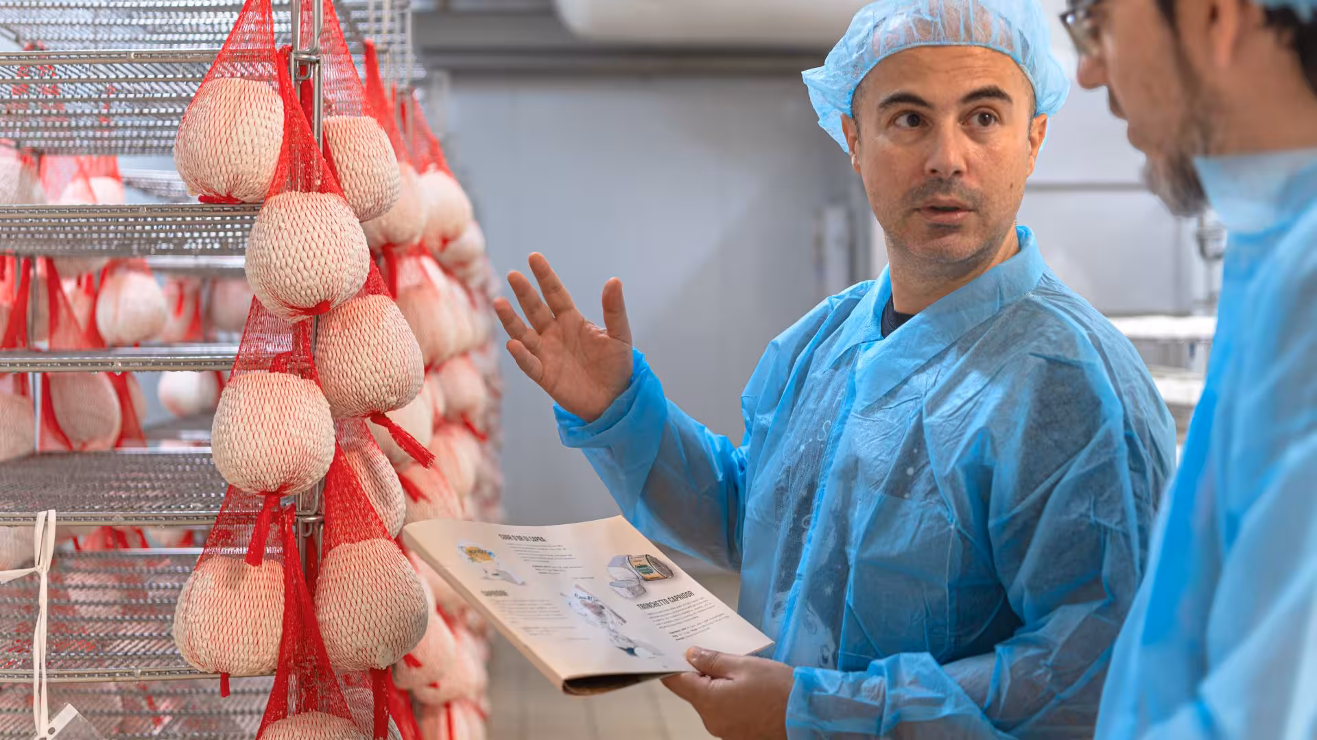Cheese expert explaining production process in Dolianova factory tour, showcasing hanging cheese rounds.