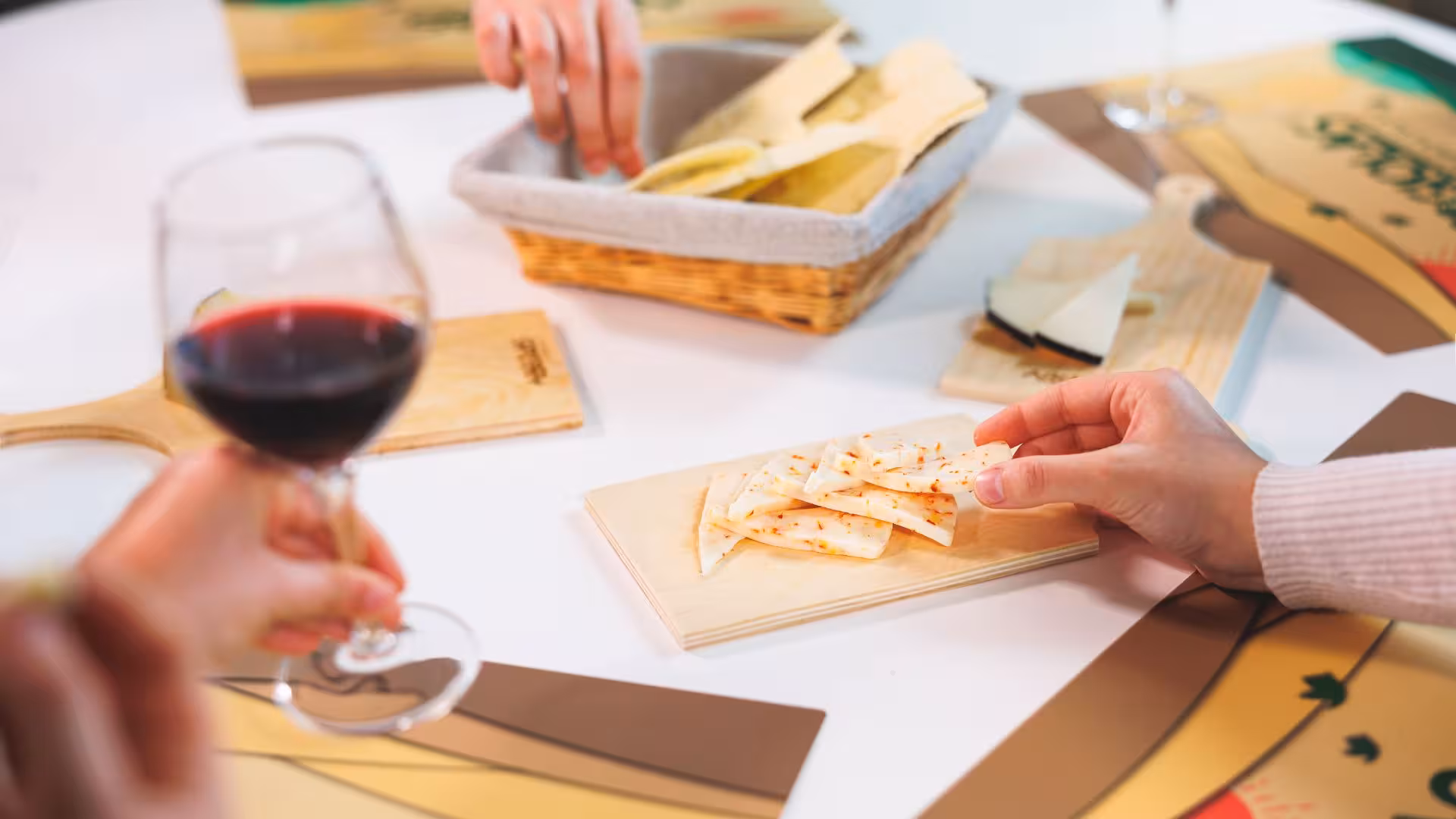 Close-up of hands sampling spicy cheese slices with red wine at Dolianova cheese factory tour.
