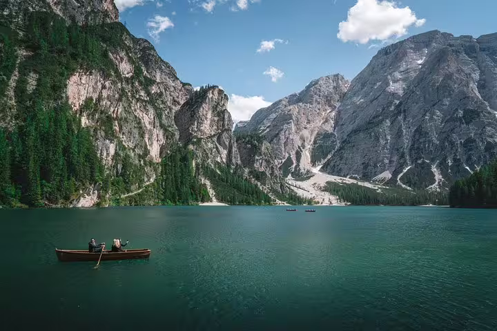 Scenic view of a boat on a tranquil lake surrounded by majestic Dolomite mountains, perfect for a day trip from Venice.