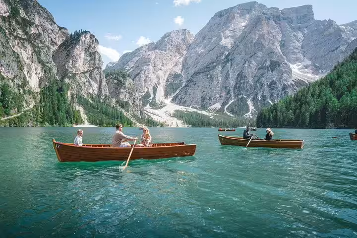 Tourists enjoy rowing boats on a serene lake with majestic Dolomites backdrop, ideal for a day trip from Venice.
