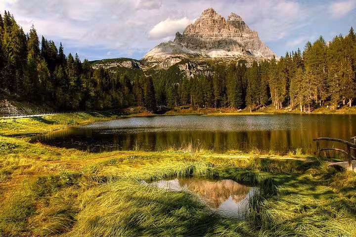 Scenic view of Italy's Dolomites with lush green meadow, tranquil lake, and majestic mountain backdrop from Venice tour.