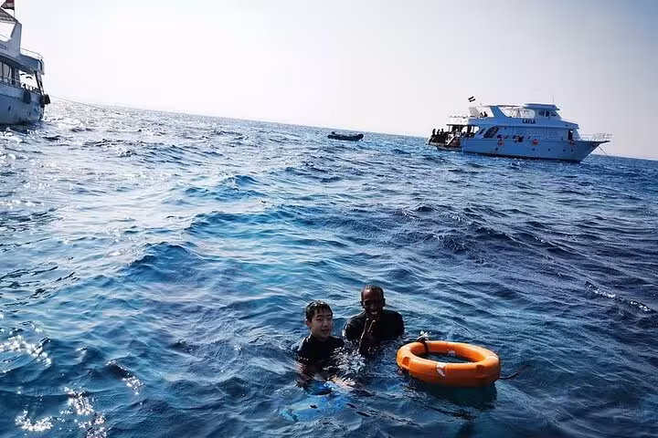 Swimmers in Red Sea with life ring near boat on Dolphin House National Park full-day snorkeling excursion