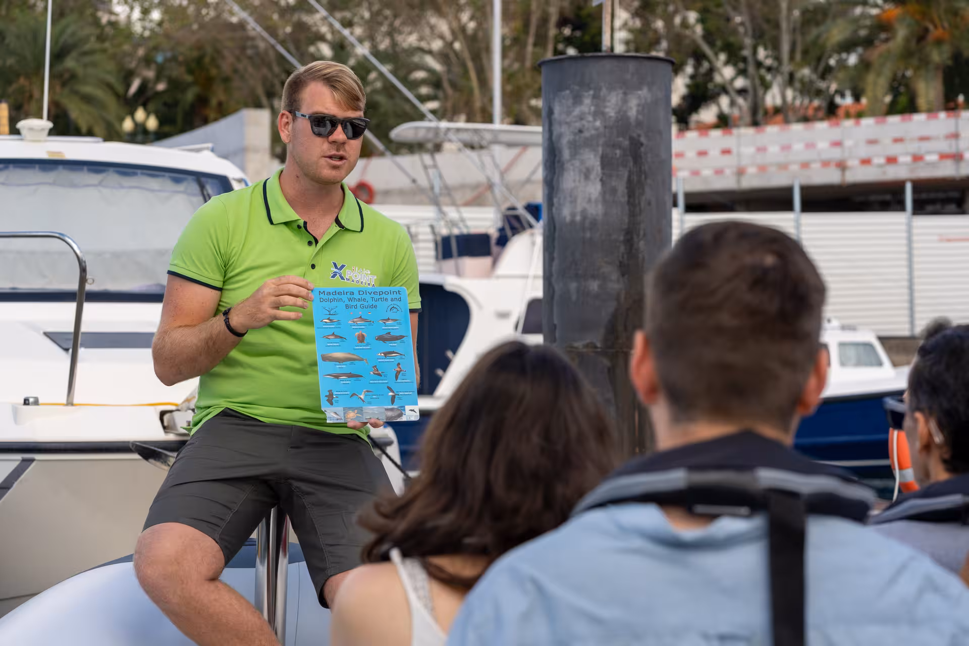 Tour guide discussing dolphin and whale tour details with guests by a RIB boat at the marina.