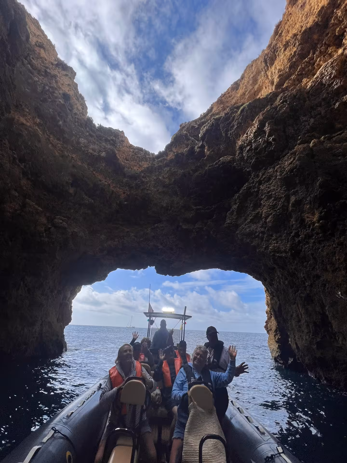 RIB boat tour guests wave while cruising through a dramatic sea cave arch at Ponta da Piedade, Lagos Algarve coast