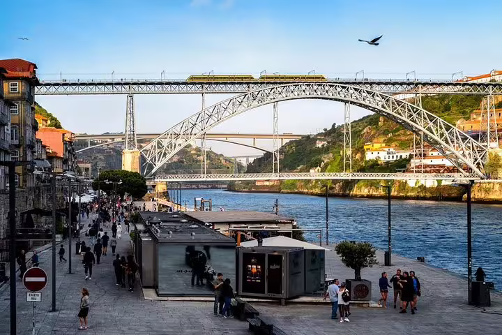 View of Porto's iconic Dom Luís I Bridge over the Douro River, bustling riverside promenade, ideal for private tours.
