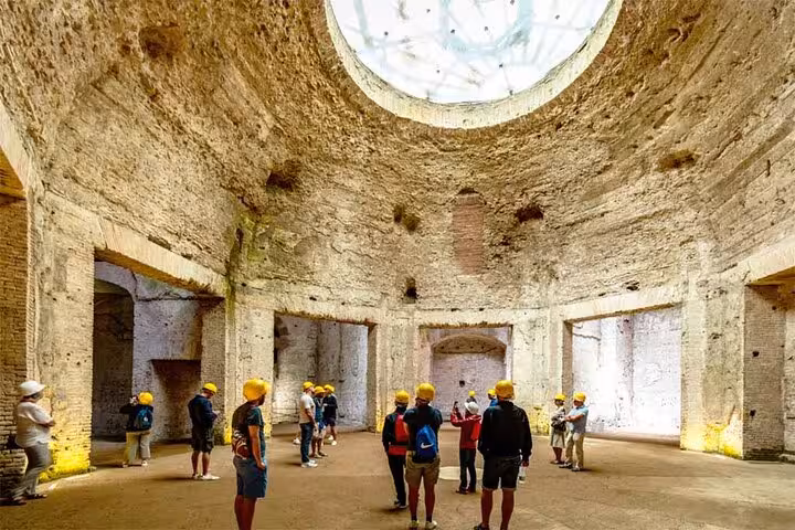 Tour group with hard hats inside the grand rotunda of Rome's Domus Aurea, illuminated by natural light.