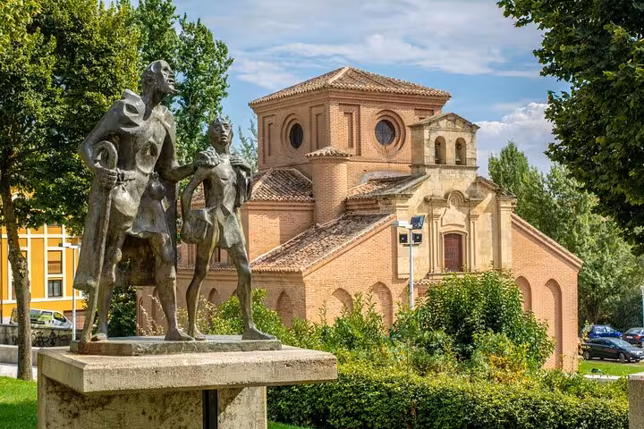 Statue of Don Quixote and Sancho Panza near a charming brick chapel surrounded by greenery in Salamanca.