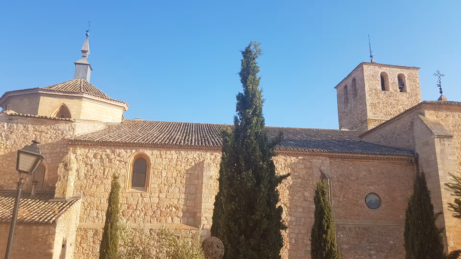 Historic stone church in La Mancha on the Don Quixote Tour, sunlit facade with cypress trees and tower