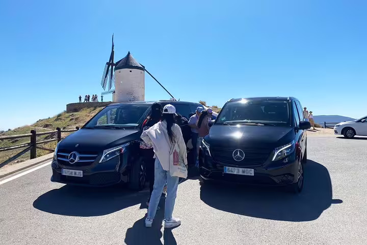 Visitors exploring the Don Quixote windmills in La Mancha, parked beside sleek Mercedes-Benz vans.