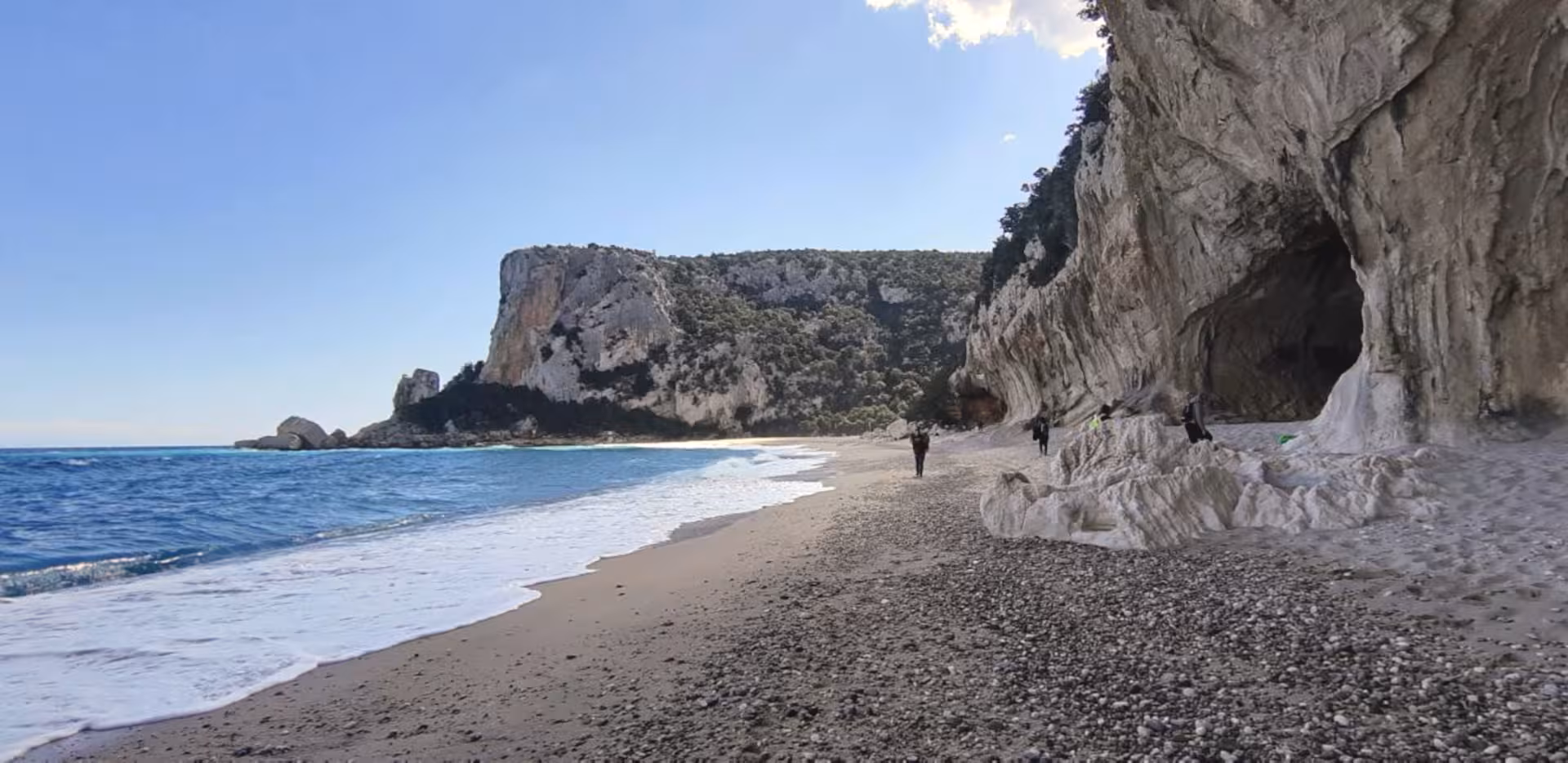 Scenic view of Cala Luna beach with turquoise sea, dramatic cliffs, and sandy shoreline under clear blue sky.