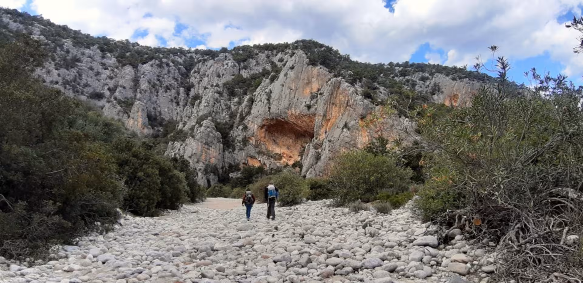 Hikers traverse rocky path surrounded by rugged limestone cliffs on the trek from Dorgali to Cala Luna.