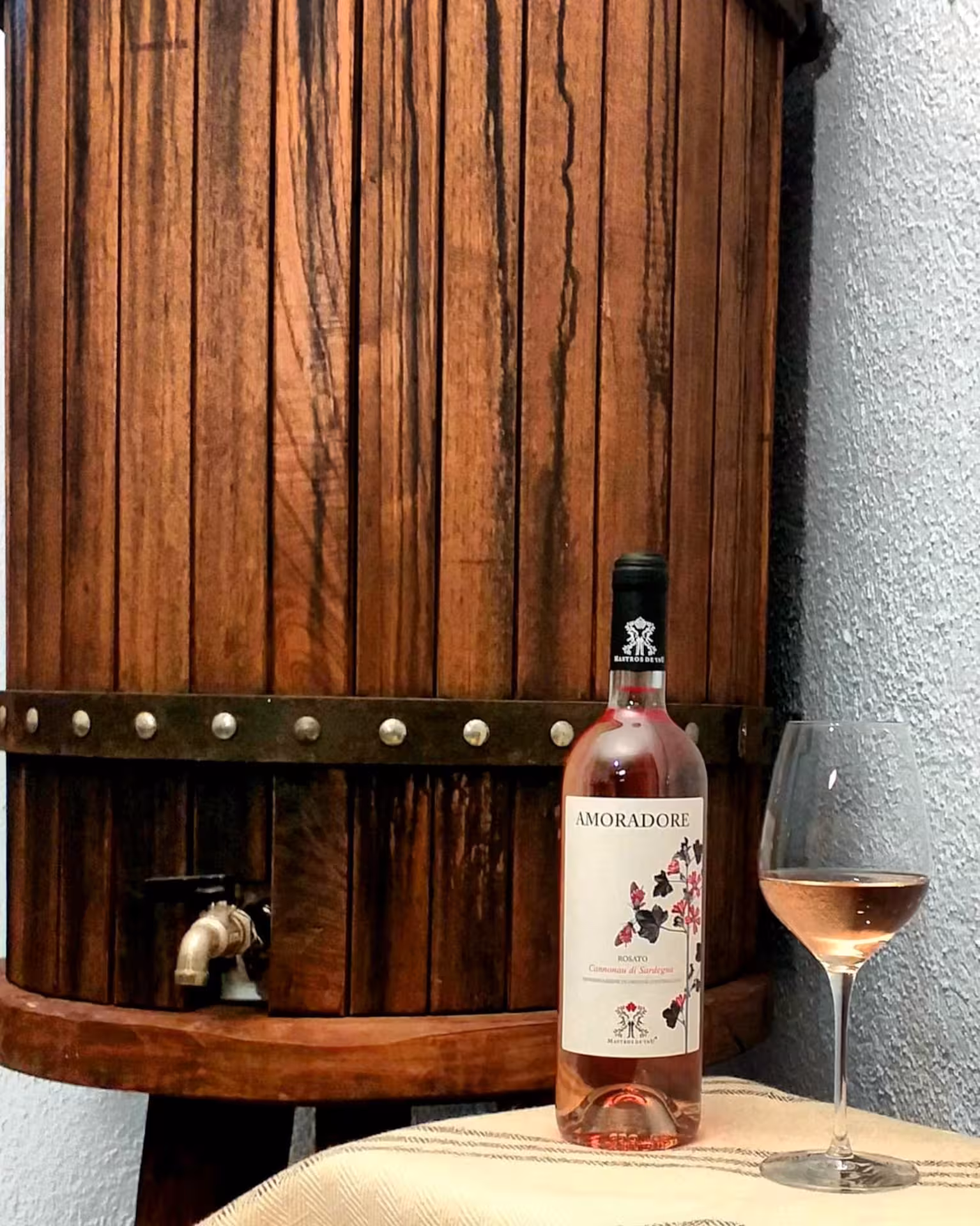 Rustic wine barrel with a bottle of Amoradore rosé and a glass at a Dorgali winery.