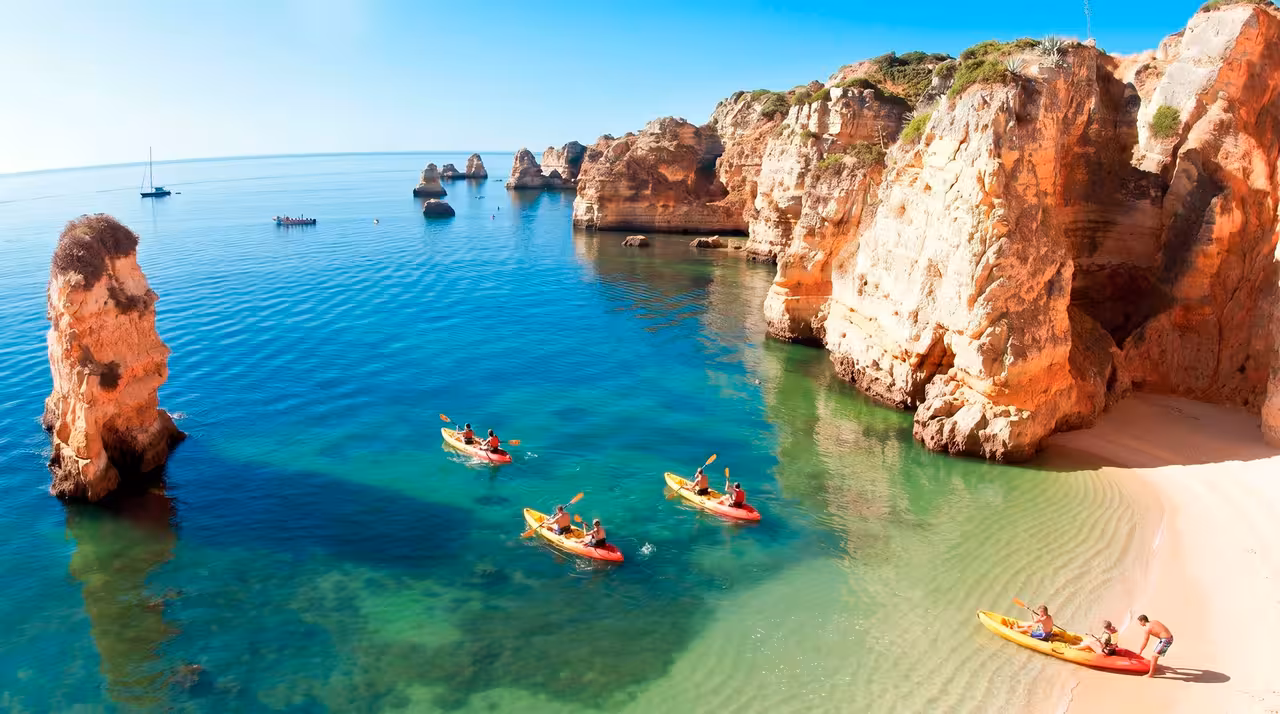 Kayakers paddling colorful kayaks near golden cliffs and turquoise waters on a private Lagos cave tour