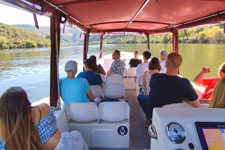 Passengers relax on guided Douro River boat tour, scenic valley views, enjoying a glass of Port wine