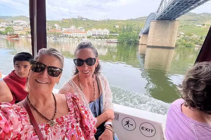 Guests smiling on a 50-minute guided Douro River boat tour near a bridge, enjoying Port wine onboard