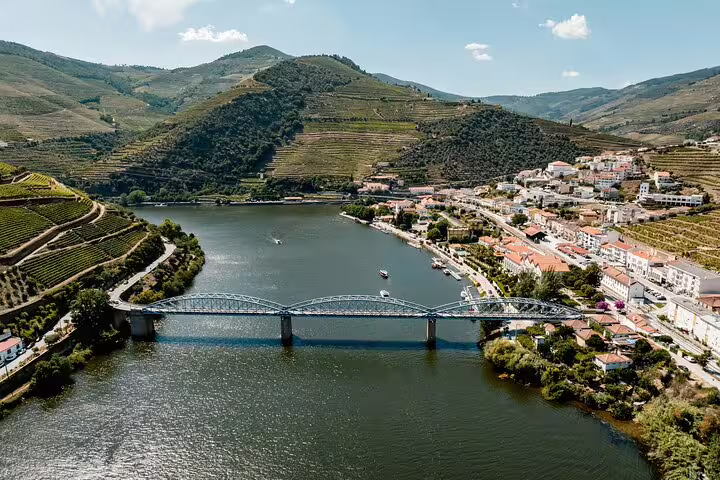 Aerial view of a bridge spanning the Douro River, with terraced vineyards and a charming village in the background.
