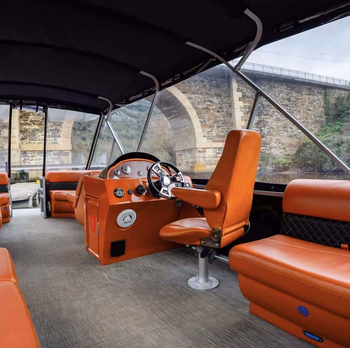 Comfortable orange leather interior of a private Douro River Valley cruise boat with historic stone bridge view