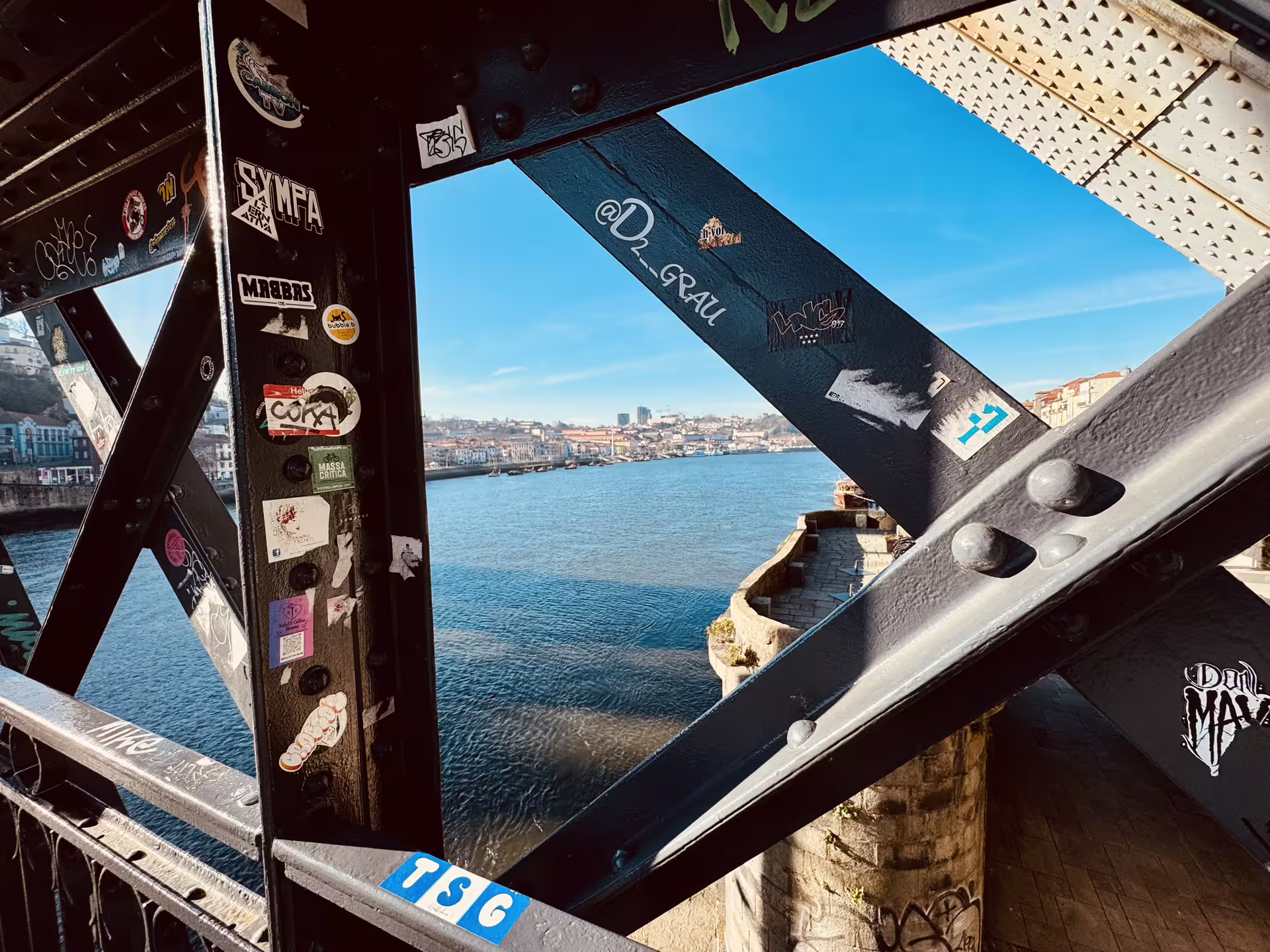 View of the Douro River from the graffiti-adorned Dom Luís I Bridge, showcasing Porto's vibrant riverside atmosphere.