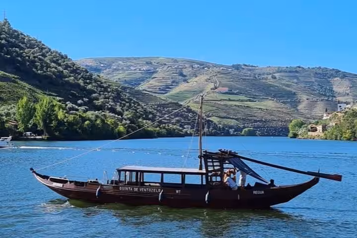 Traditional rabelo boat cruising the Douro River with terraced vineyards perfect for a Portuguese lunch tour