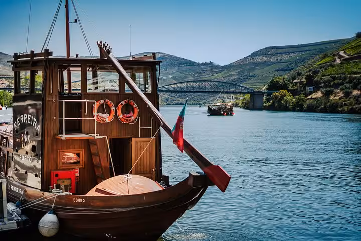 Traditional Ferreira rabelo boat on the Douro River with scenic vineyard hills and bridge in Portugal