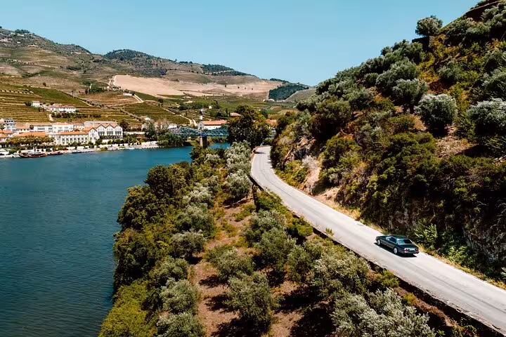 Scenic drive along the Douro River with lush vineyards and a winding road on a sunny day.
