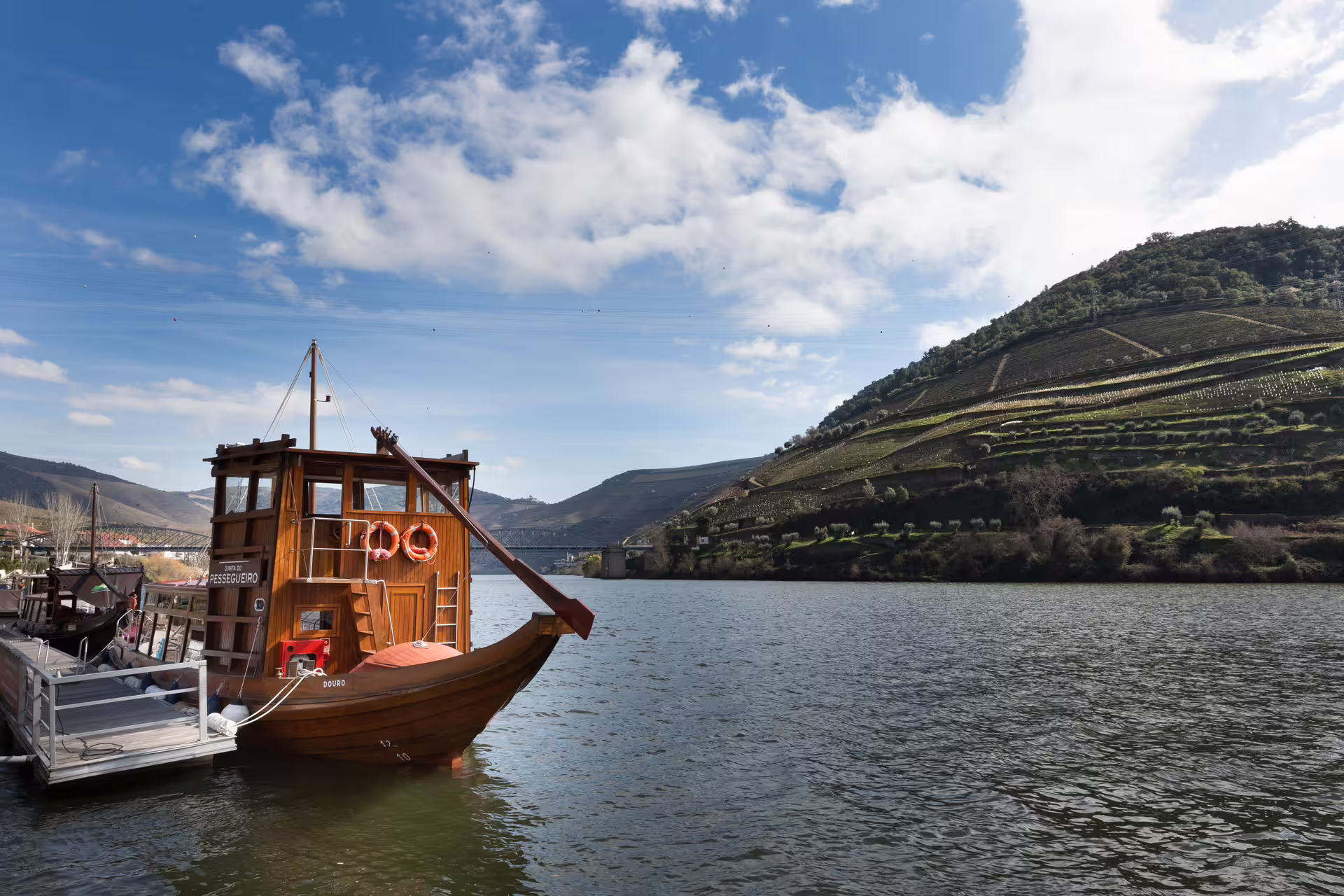 Traditional wooden boat docked on the Douro River with picturesque vineyard hills in the background.
