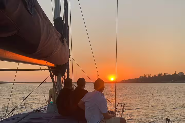 People enjoying a picturesque sunset aboard a sailboat on the Douro River in Porto, perfect for a romantic evening cruise.