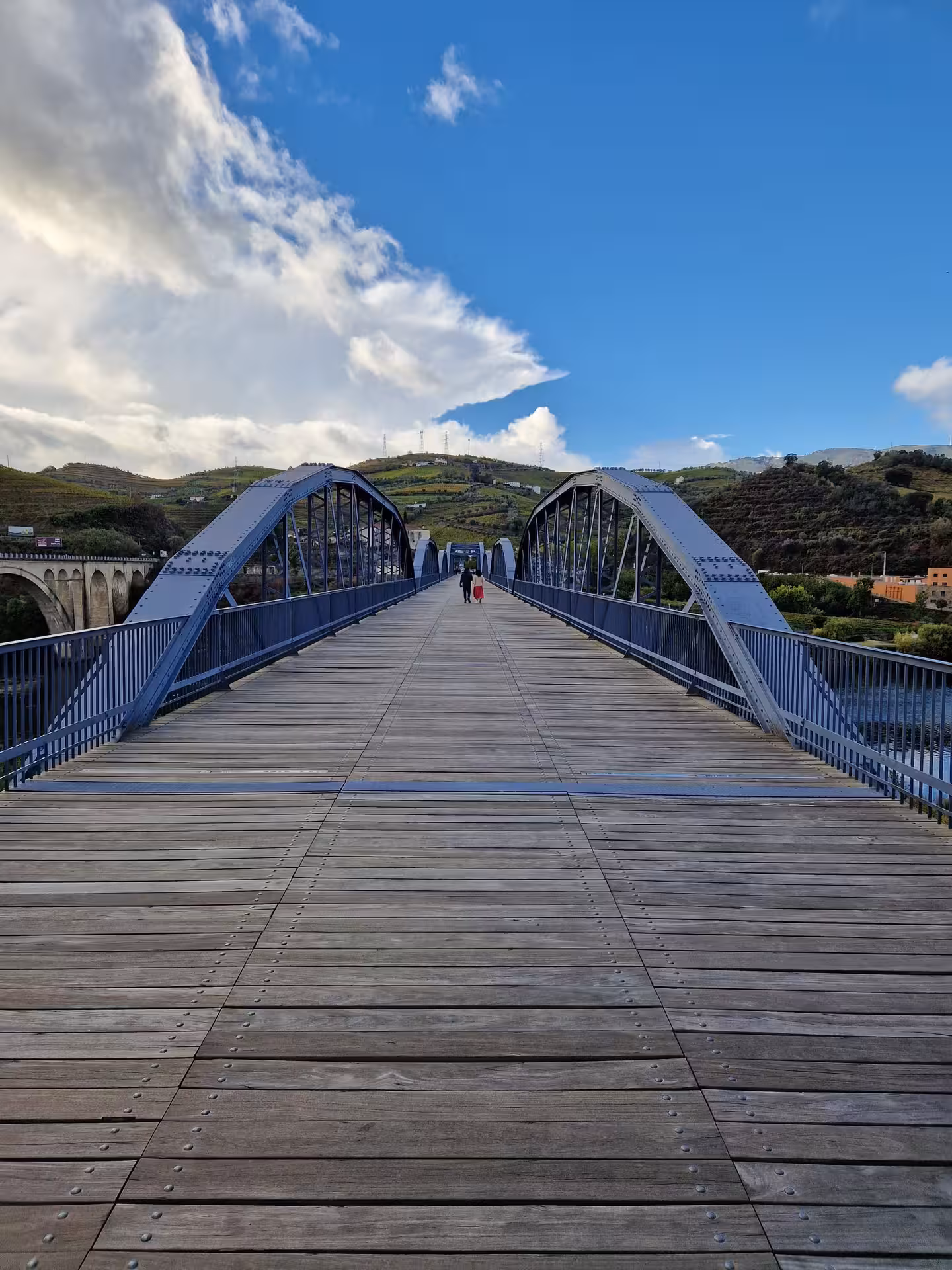 Couple walking across a wooden footbridge over the Douro River with terraced vineyards on a private valley tour