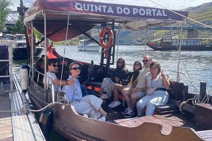 Small group cruising the Douro River on a traditional rabelo boat by terraced vineyards on a Porto wine tour with lunch.