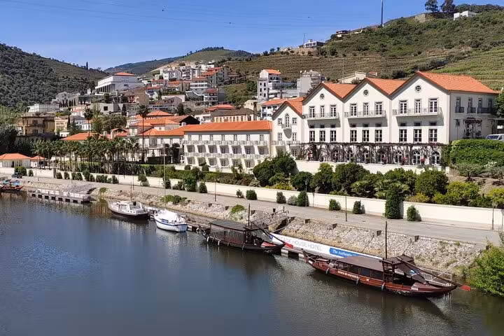 Scenic Douro Valley riverfront with traditional rabelo boats docked near a historic winery hotel and terraced vineyards