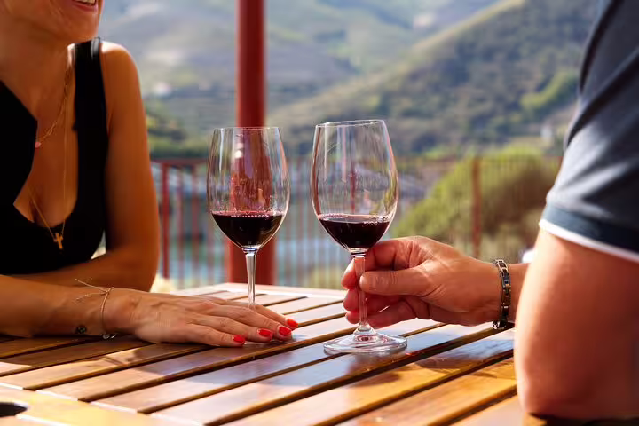 Two glasses of red wine on a wooden table with a scenic Douro Valley view, part of a wine tasting experience.