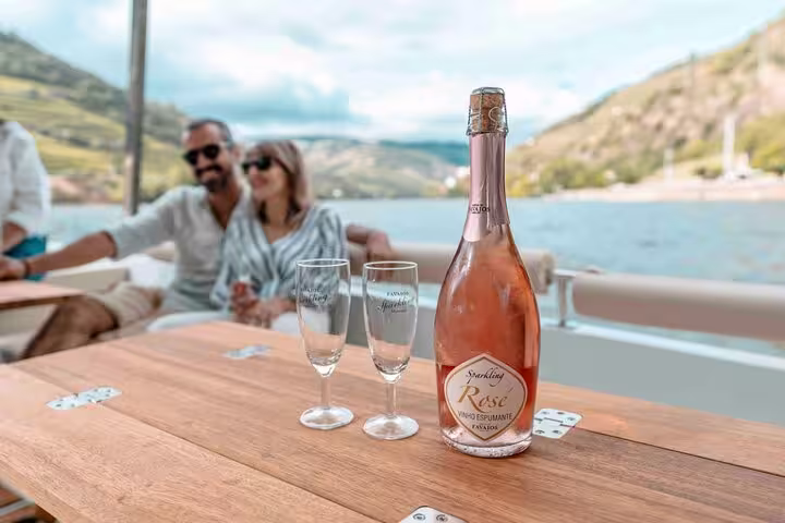 Bottle of sparkling rosé and glasses on a boat table during a Douro Valley wine tasting tour.