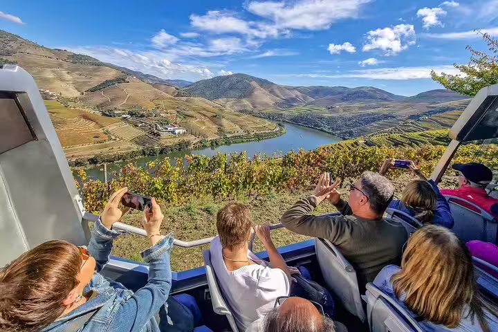 Tourists enjoying panoramic views of the Douro Valley vineyards and river from a scenic vantage point during a private transfer to Lisbon.