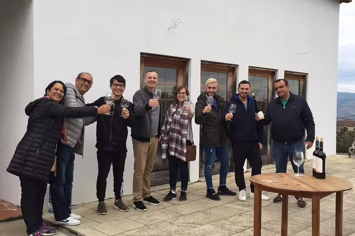 Group of tourists enjoying wine tasting experience on a sunny terrace in Douro Valley, Portugal.