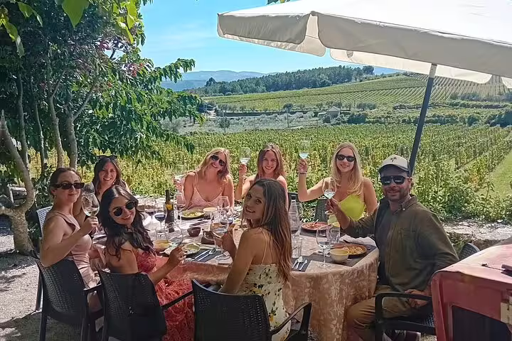 Group enjoying wine tasting and lunch at a scenic Douro Valley vineyard with lush vineyards in the background.