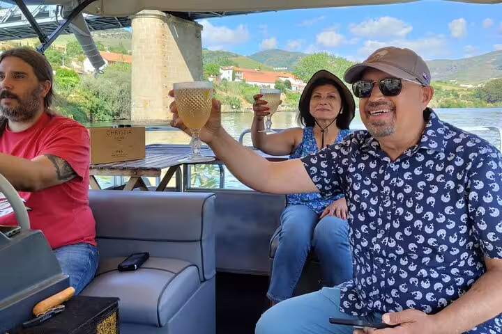 Tourists raising glasses on a relaxing Douro River boat cruise, surrounded by stunning valley views.