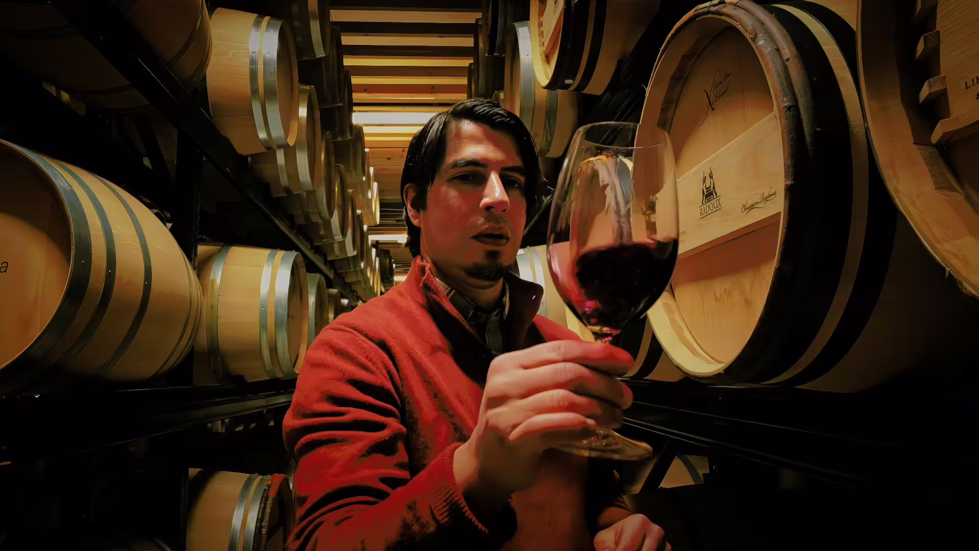 Man examining a glass of red wine in a Douro Valley cellar surrounded by oak barrels.