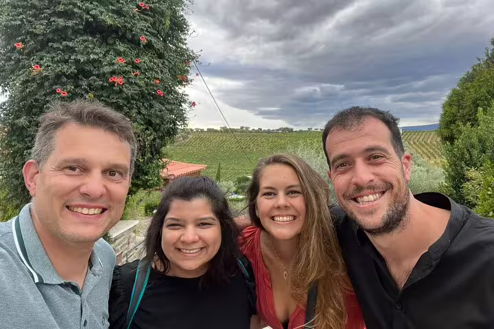 Group of smiling tourists posing in Douro Valley vineyard with lush greenery and cloudy skies, ideal for a private wine tour.