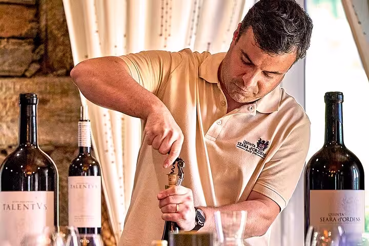 Winemaker opening wine bottle in Douro Valley, highlighting sustainable wine tour experience with local flavors.