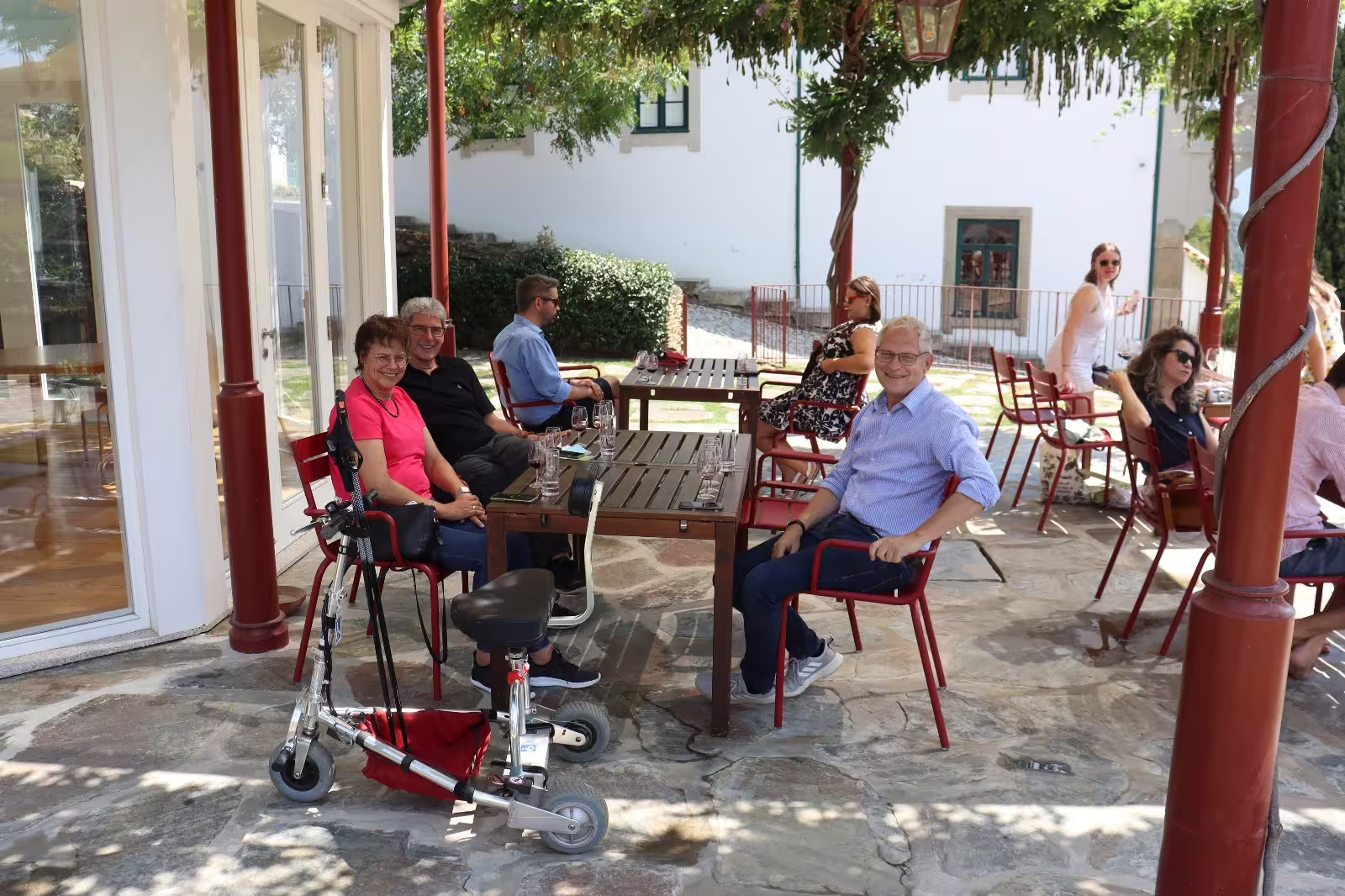 Visitors enjoying a sunny day at a winery patio in Douro Valley on a private tour, surrounded by scenic views and wine glasses.