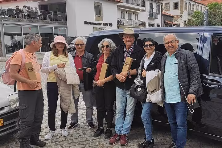 Tour group posing with wine boxes by a van in a Douro Valley village after a guided winery excursion