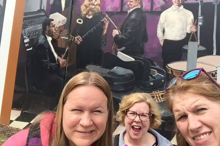 Three women smiling in front of a colorful music mural during a downtown Atlanta walking tour