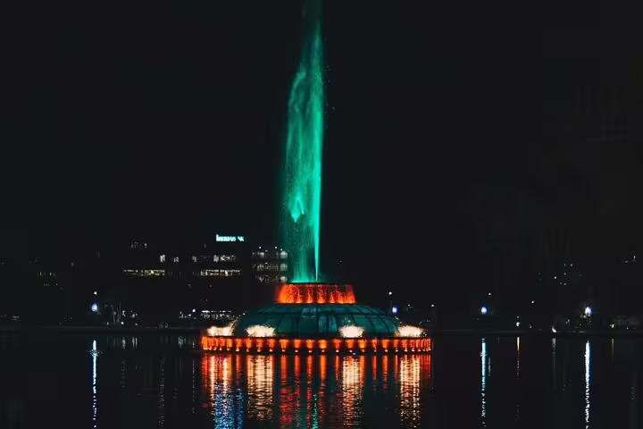 Illuminated fountain with green and orange lights reflected on water at night in Downtown Orlando