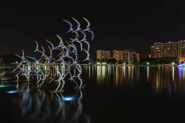 Illuminated bird sculptures at night over a reflective lake in Downtown Orlando