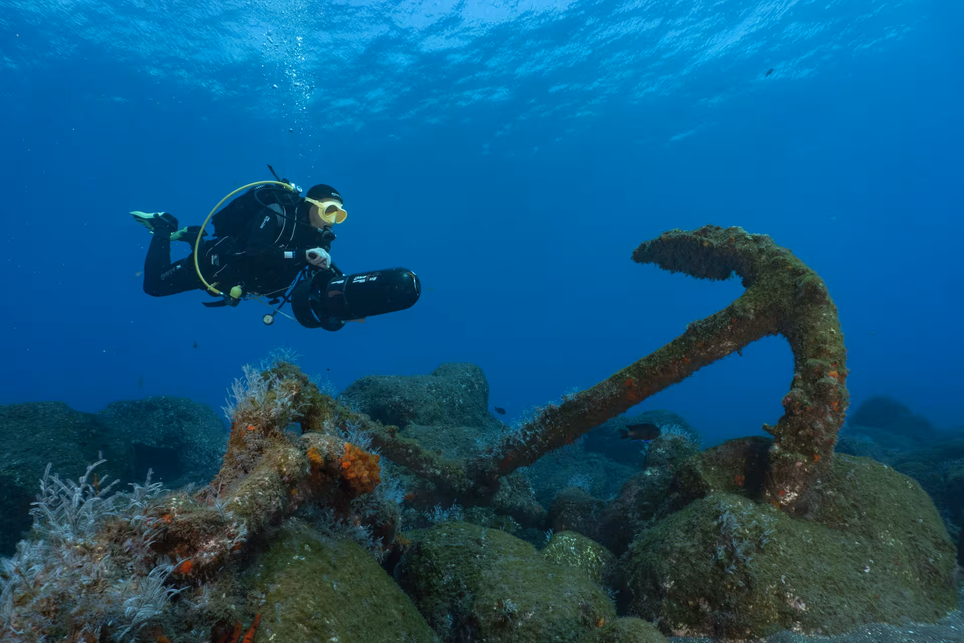 Diver explores underwater anchor with DPV scooter, showcasing thrilling scooter dive adventure in vibrant marine setting.