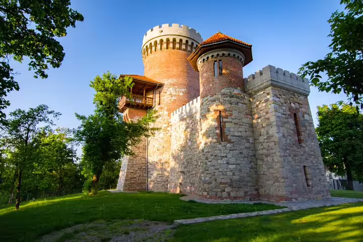 Medieval stone castle with round brick towers and battlements surrounded by green trees in Bucharest