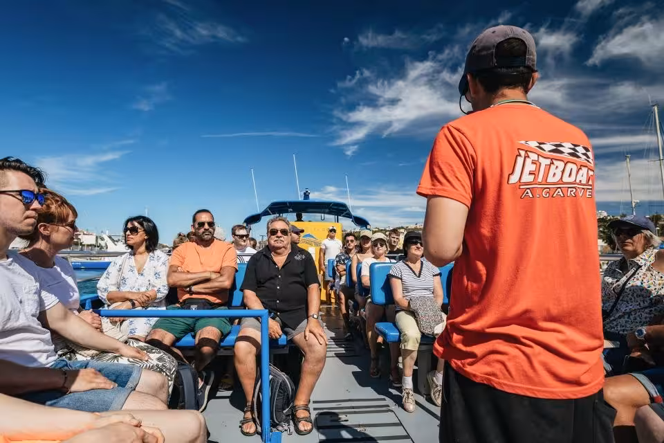 Tour guide briefing excited passengers on a sunny boat deck, setting sail for the Dreamer Caves & Dolphin Watching experience.