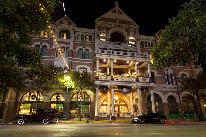 The Driskill Hotel illuminated at night in Austin, Texas, with vintage cars parked outside