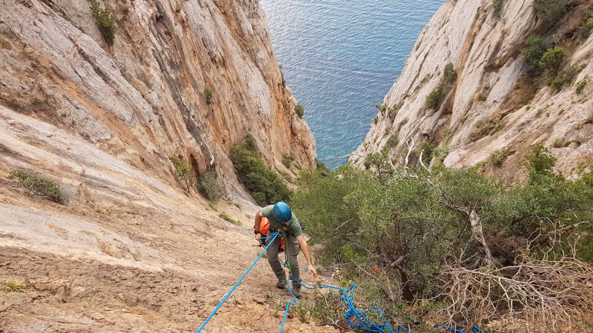 Adventurer ascending a steep cliff in Porto Flavia, showcasing dry canyoning with safety gear and stunning sea view.