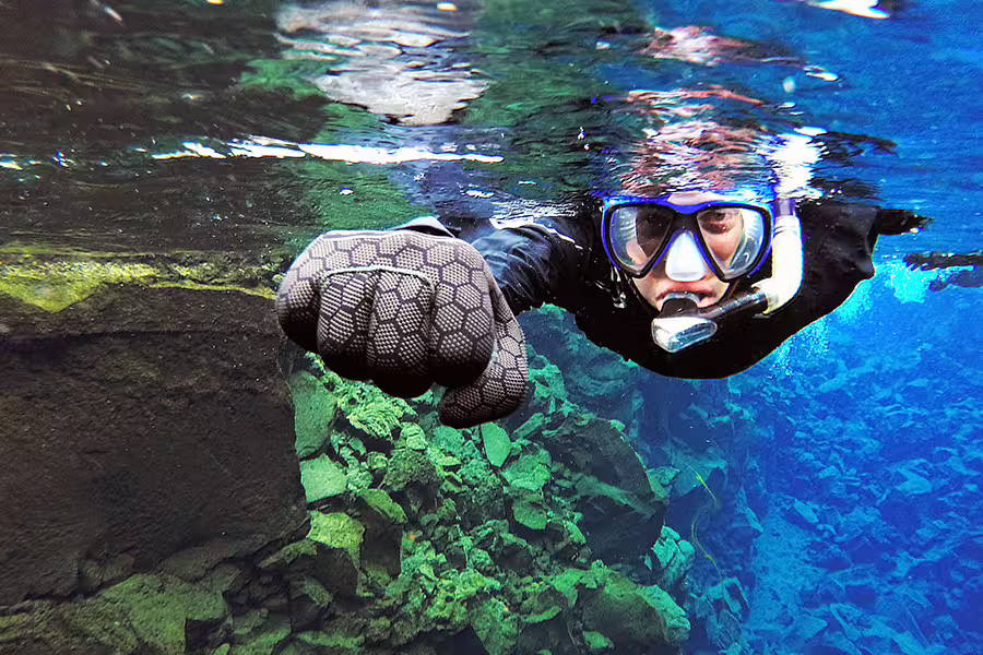Snorkeler in a drysuit explores the crystal-clear waters of Silfra, capturing vibrant underwater photos in Iceland's unique rift.